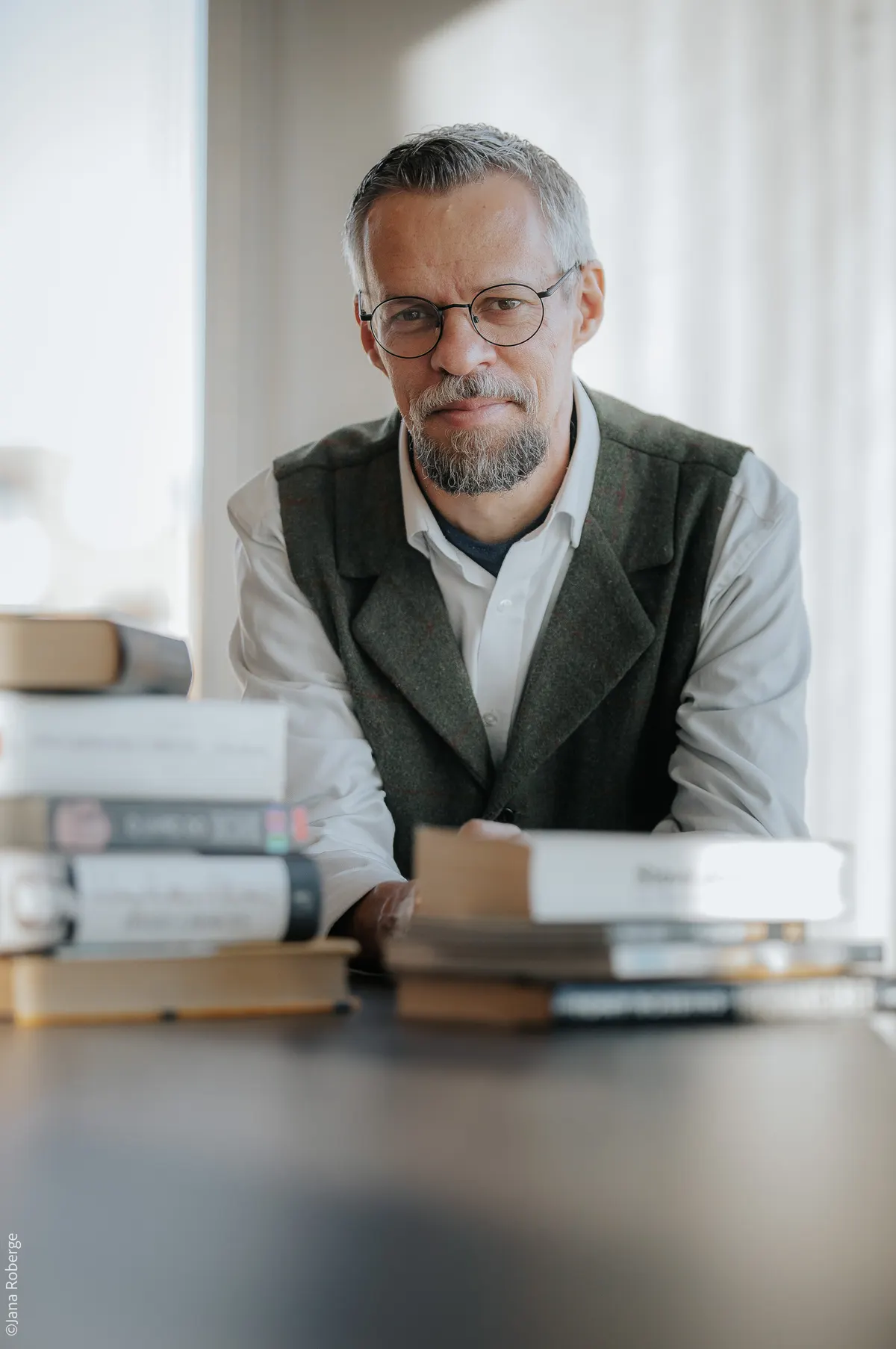 Sandro Vitta à mesa, entre pilhas de livros